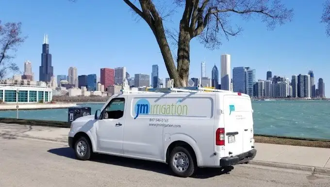 White van with JM Irrigation logo parked by lake with Chicago skyline in background