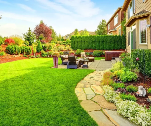 A backyard with green lawn, stone patio, and hot tub.